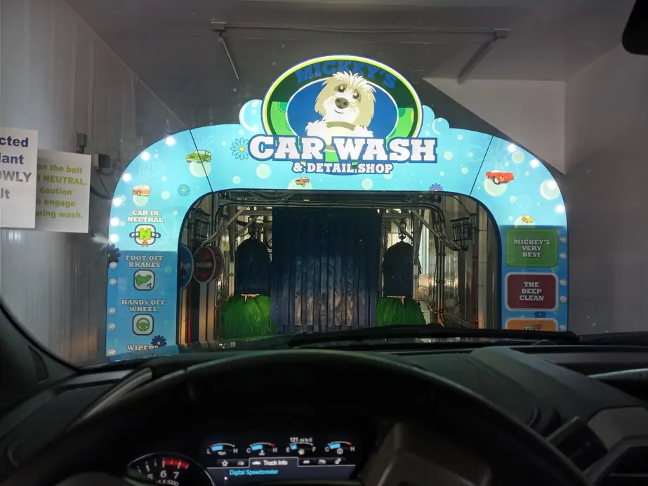 Driver's view of the tunnel entry arch with the shaggy grey-and-white dog logo above the wash menu panels