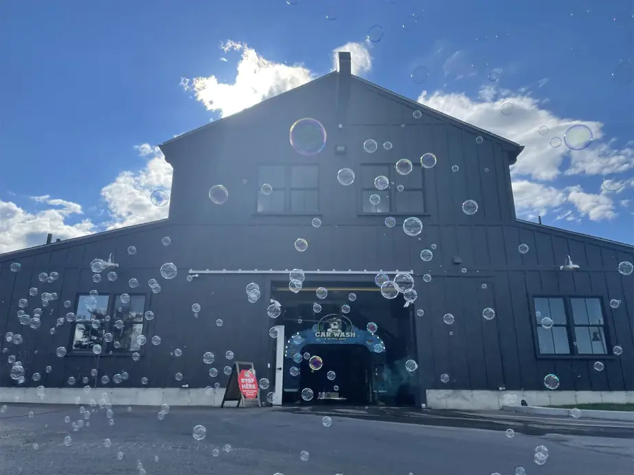 The black board-and-batten barn at Mickey's Car Wash with soap bubbles drifting across the front and the dog arch visible inside